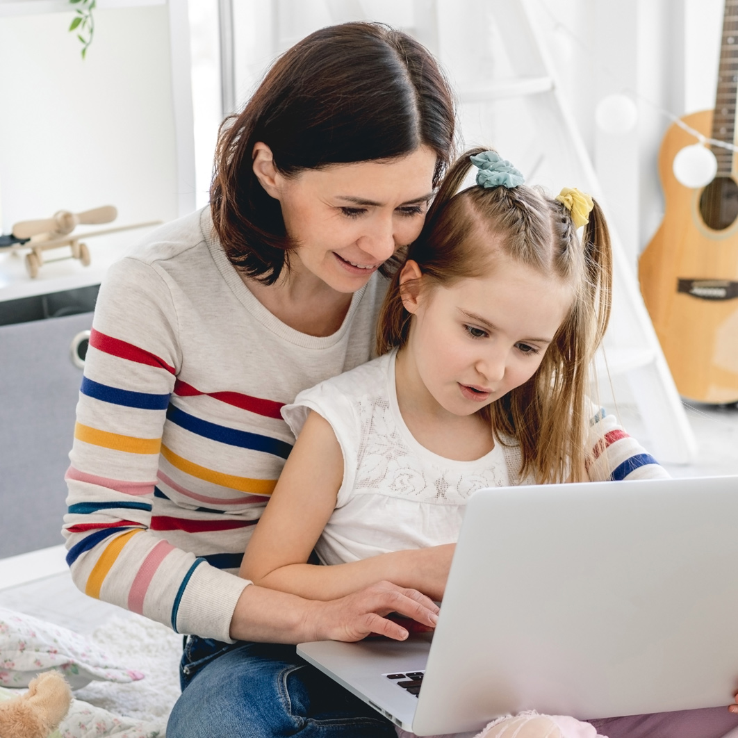 Young girl sitting on a woman's lap looking at a computer together