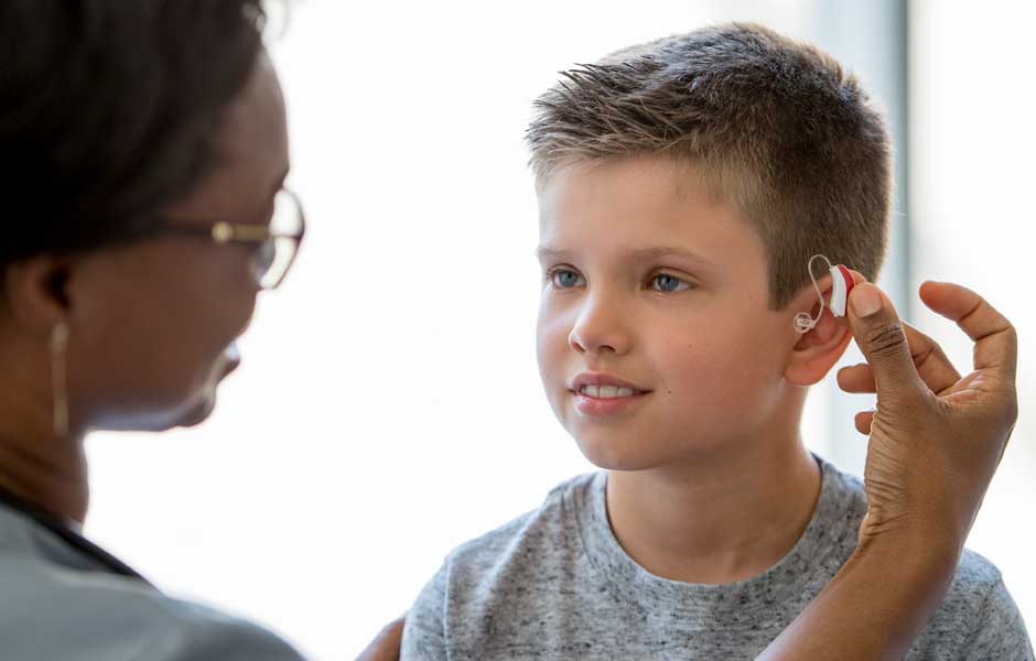 A female doctor puts a hearing aid on a boy's ear to see how it fits.