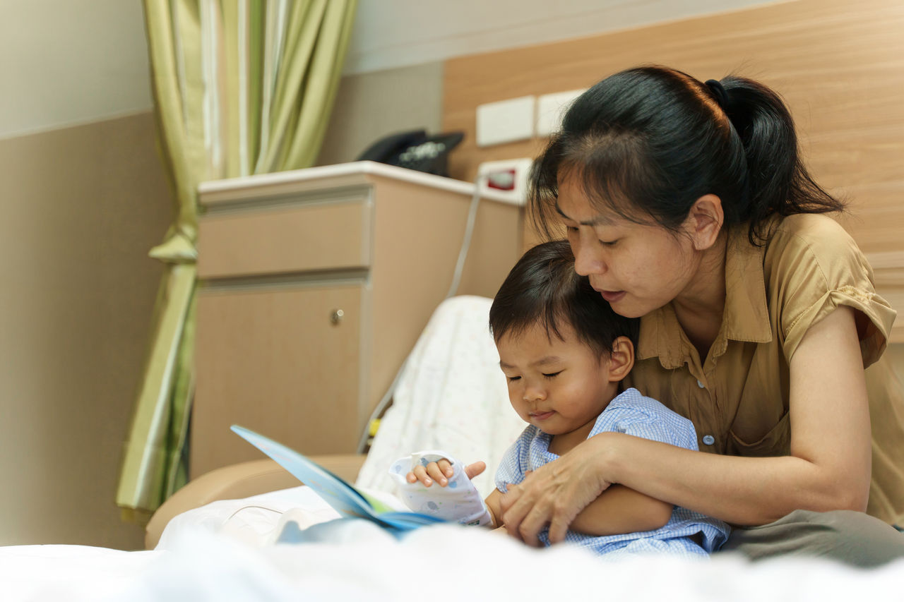 Adorable Asian kids get sick from virus be take care and read a book with his mother received antibiotic medicine and infusion saline in hospital wait for recovery. Baby health care medical concept.