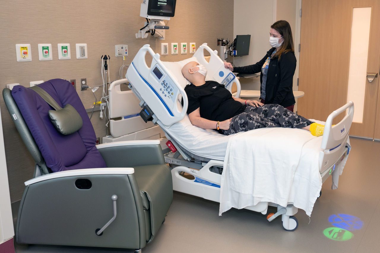 A sick teenager laying in a hospital bed speaking with a nurse