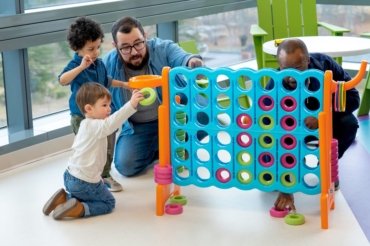 Two fathers and their sons playing a large version of connect four