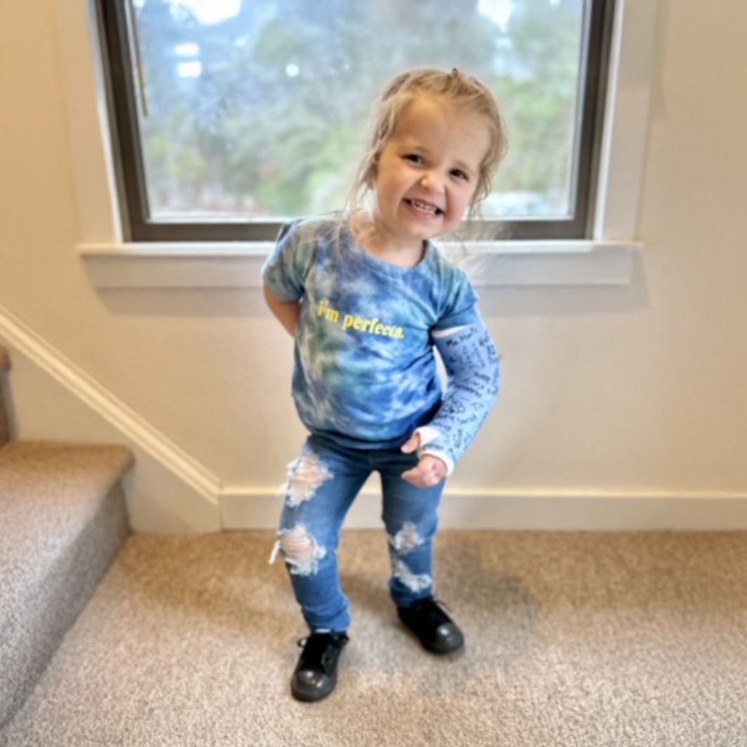 Young girl wearing a blue cast smiling at the bottom of a staircase