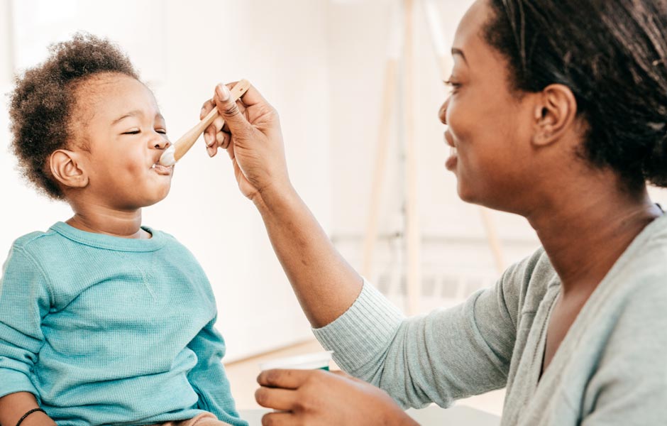 Young mom feeds her toddler with a spoon. 